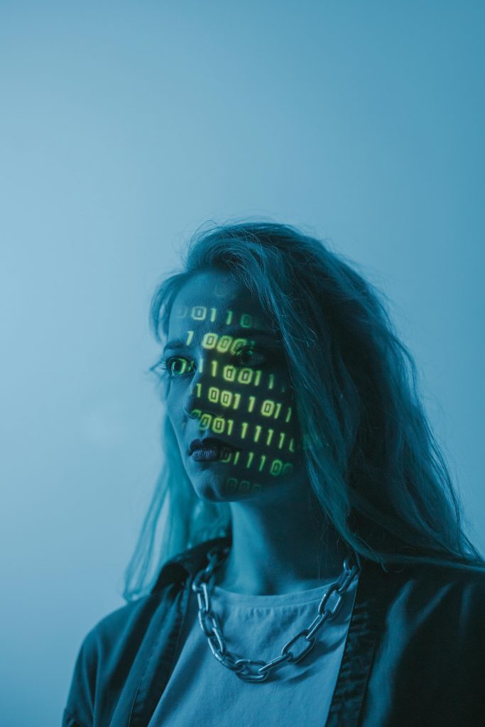 Proton VPN Review Image. This image features the ProtonVPN review. It shows a blond lady in a blue-lighted room, green code reflected on her face. 